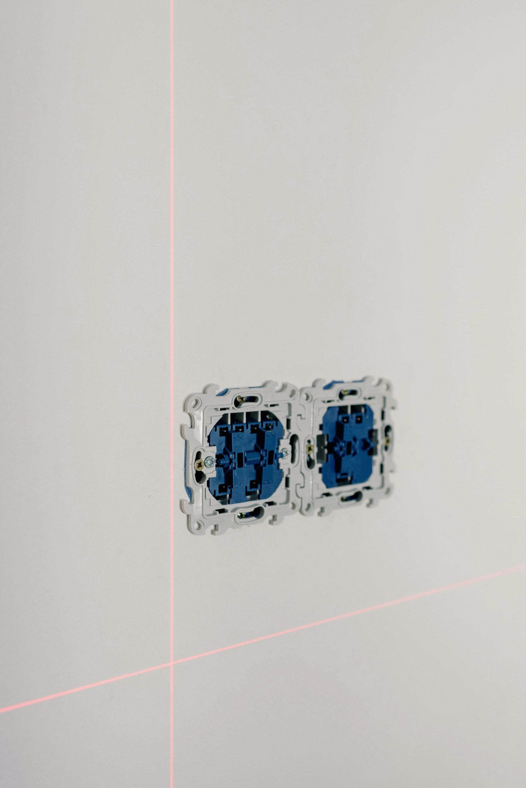 Close-up of an electrical socket installation with laser alignment lines in a minimalist interior.